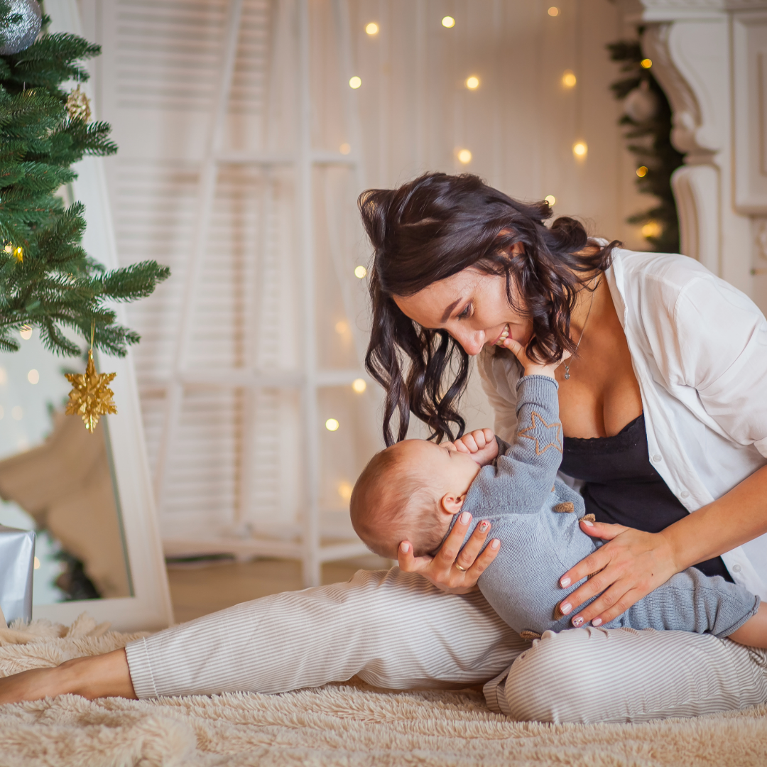 yBreastfeeding mum feeding baby at christmas next to christmas tree